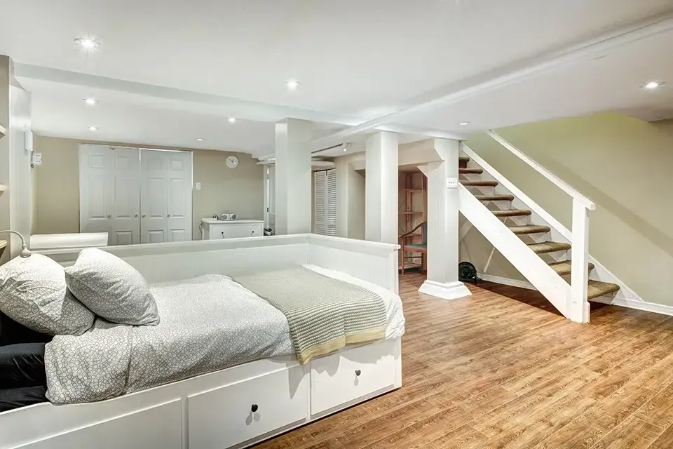 A bedroom in a basement with a bed and stairs.
