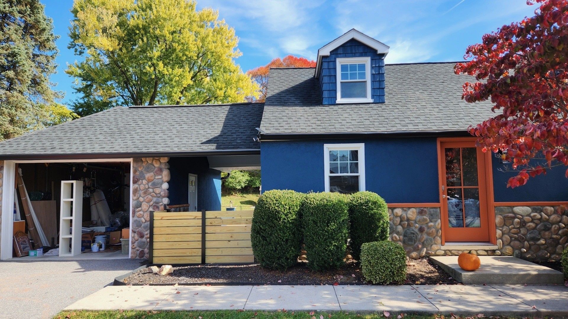 Blue house with orange door, stone accents, and small garage, under a blue sky.