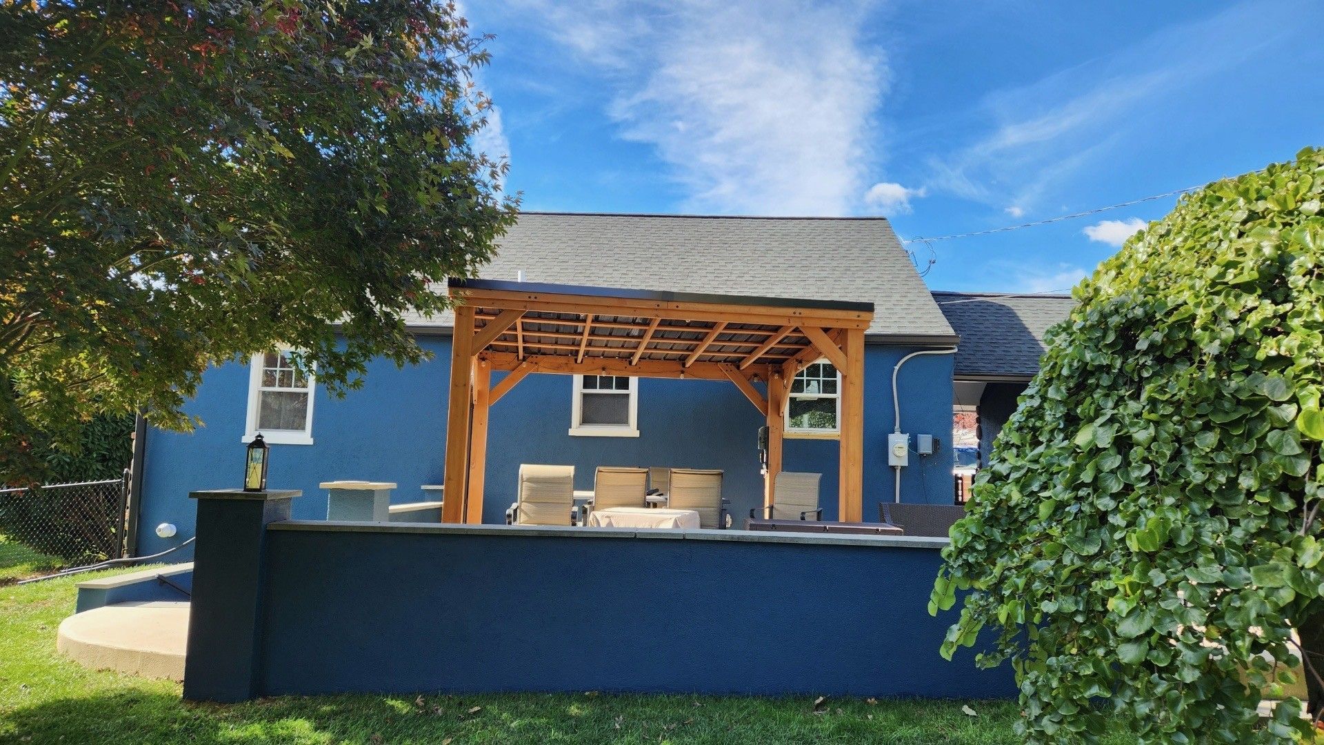 Blue house with wooden pergola over patio, clear sky.