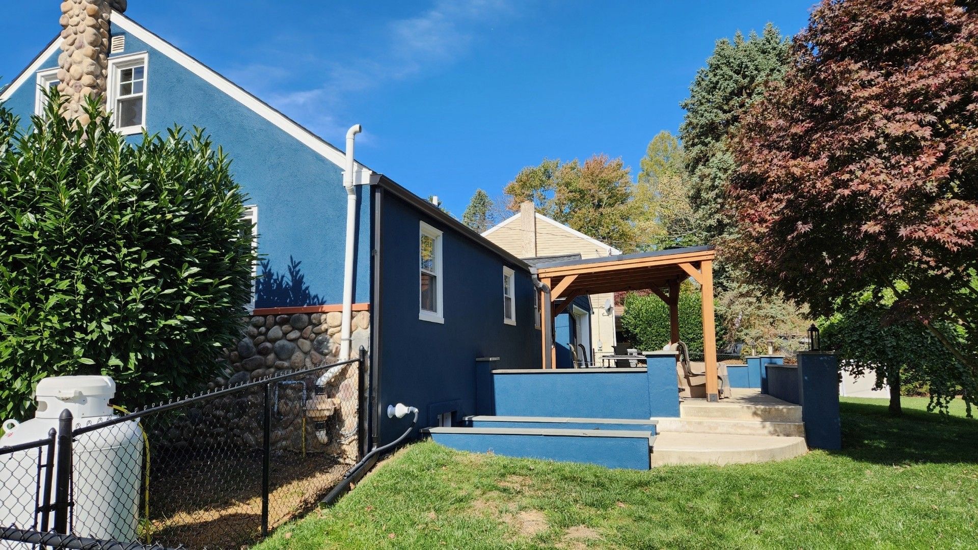 Blue house with a wooden pergola, steps, and black fence on a sunny day.