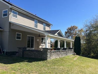 Back of a two story beige house with a covered patio. The patio has stone walls, white columns, and is on a grassy lawn.