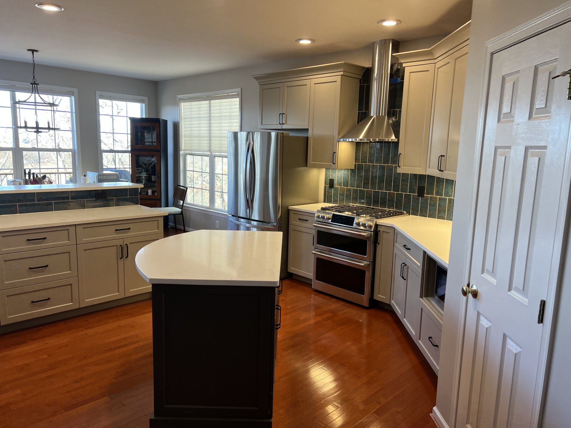 Modern kitchen with white cabinetry, a dark island, stainless steel appliances, and wood flooring.