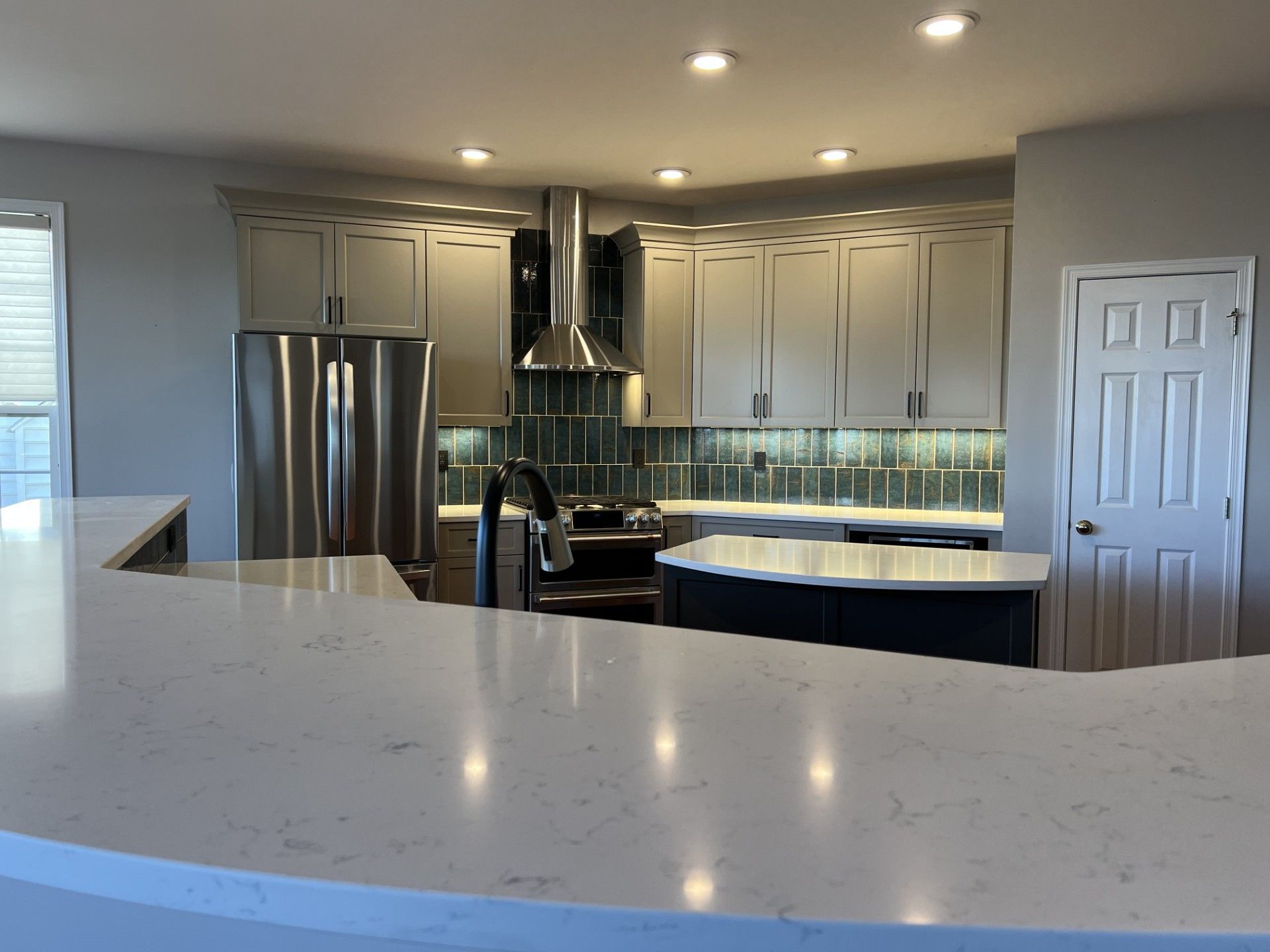 Modern kitchen with stainless steel appliances, gray cabinets, and a white countertop.
