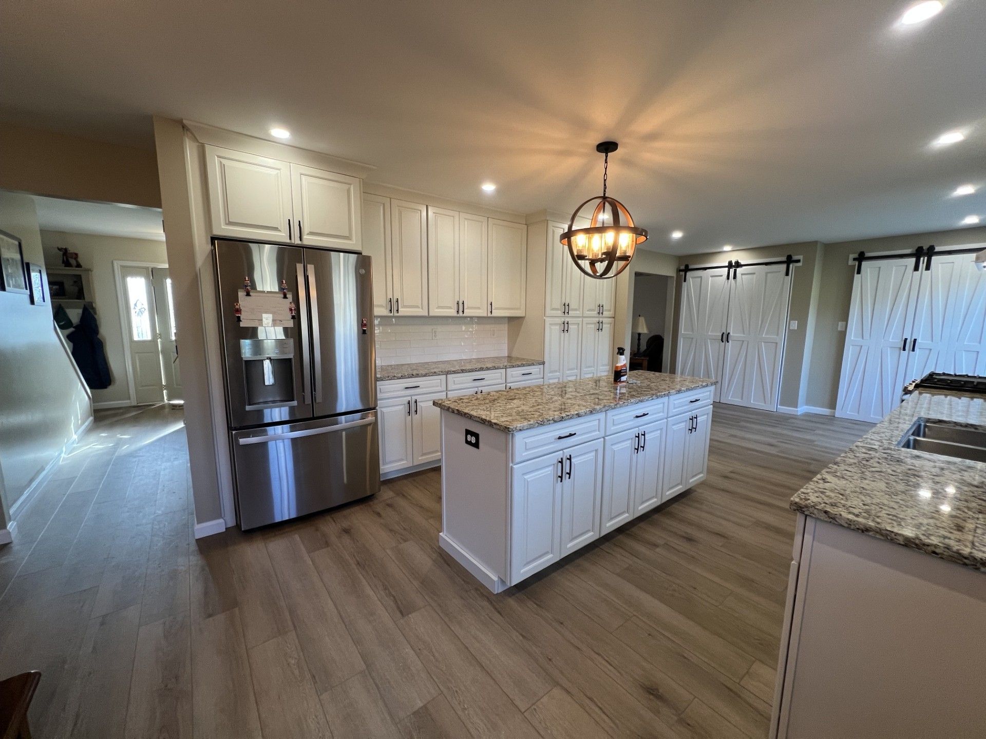 Modern kitchen with white cabinets, island, stainless steel fridge, and wood floors. 