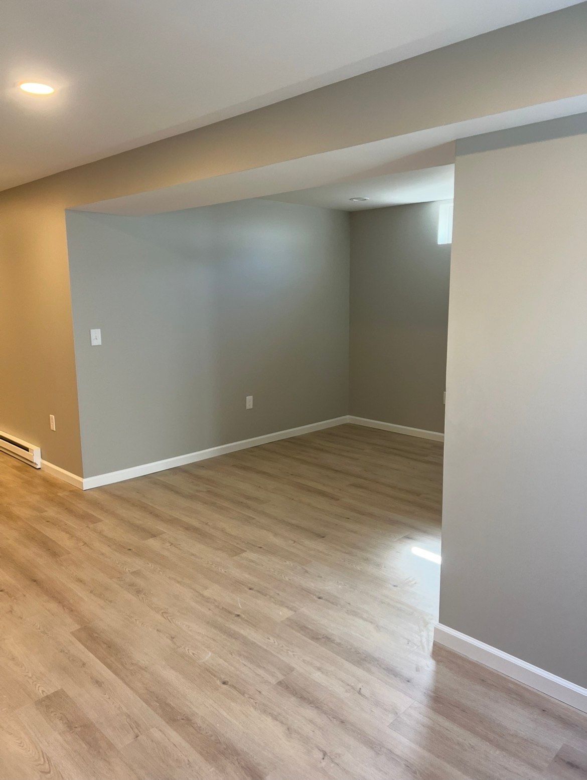 Empty finished basement with light wood-look flooring and gray walls; recessed lighting.