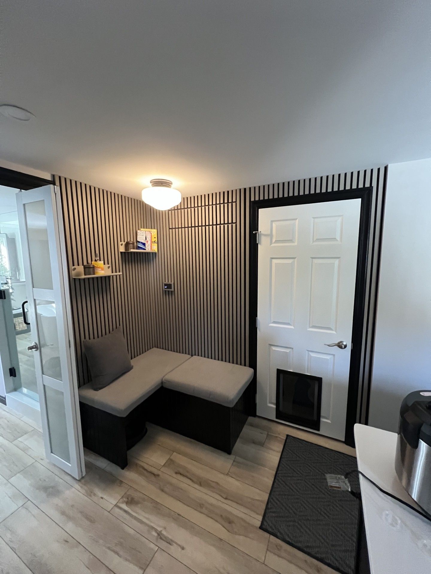 A small entryway with a built-in bench, vertical striped wall, a door with a pet door, and a floating shelf.