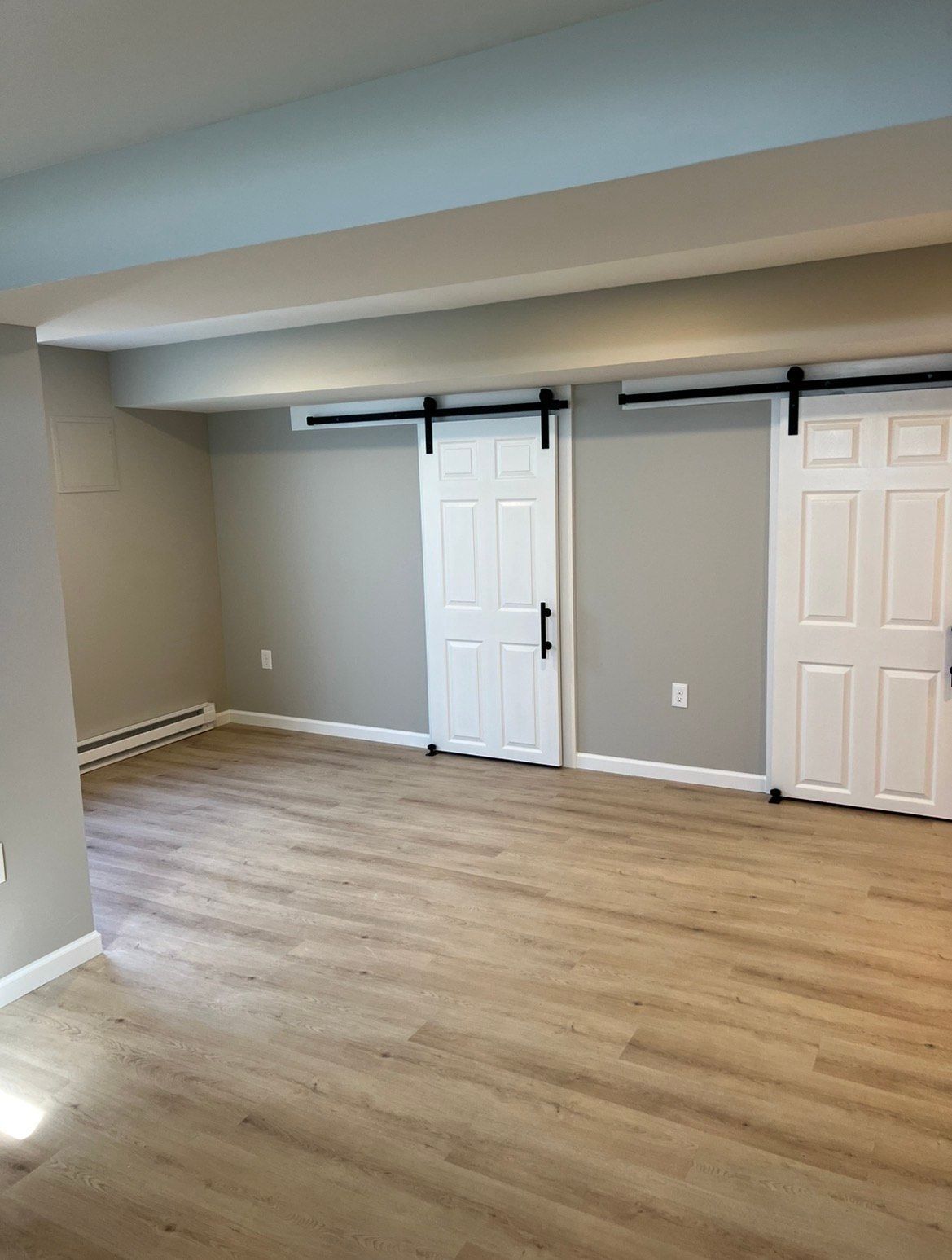 Empty room with light wood flooring, gray walls, and two white barn doors.