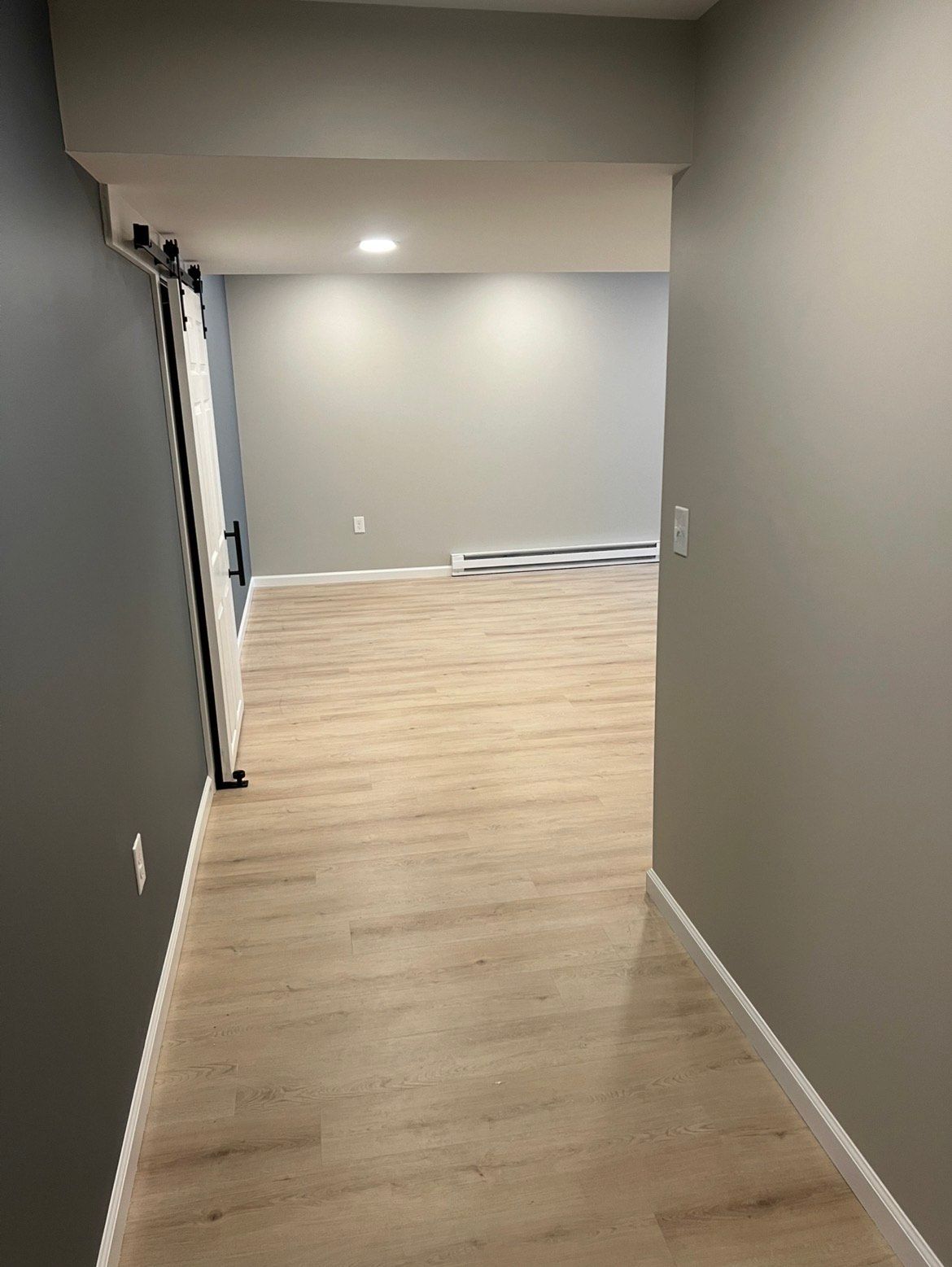 Hallway with light wood flooring, gray walls, and a sliding barn door.