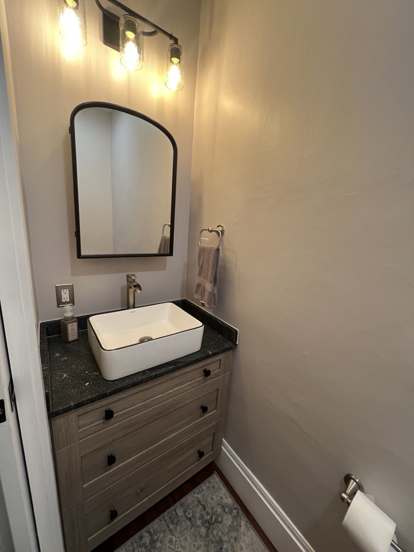 Bathroom with vanity, sink, and mirror, featuring a black and white aesthetic and a grey wall.