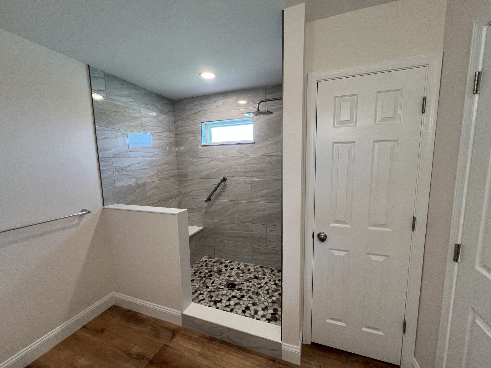 Bathroom with tiled shower, pebble floor, glass enclosure, white door, and wood-look floor.