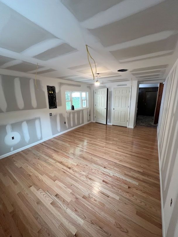 An empty room with hardwood floors and drywall on the walls.