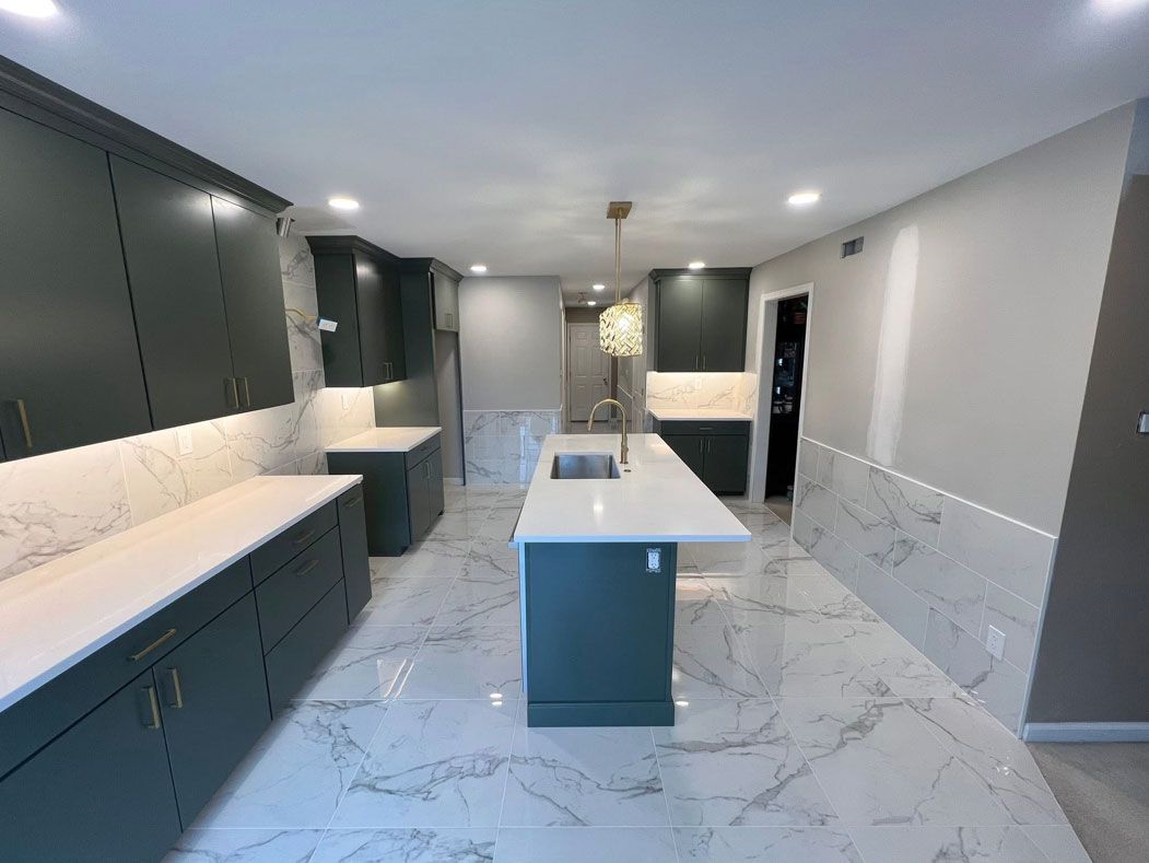 A kitchen with green cabinets , white counter tops , and a large island.