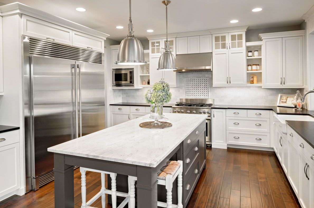 A kitchen with white cabinets and stainless steel appliances and a large island in the middle.