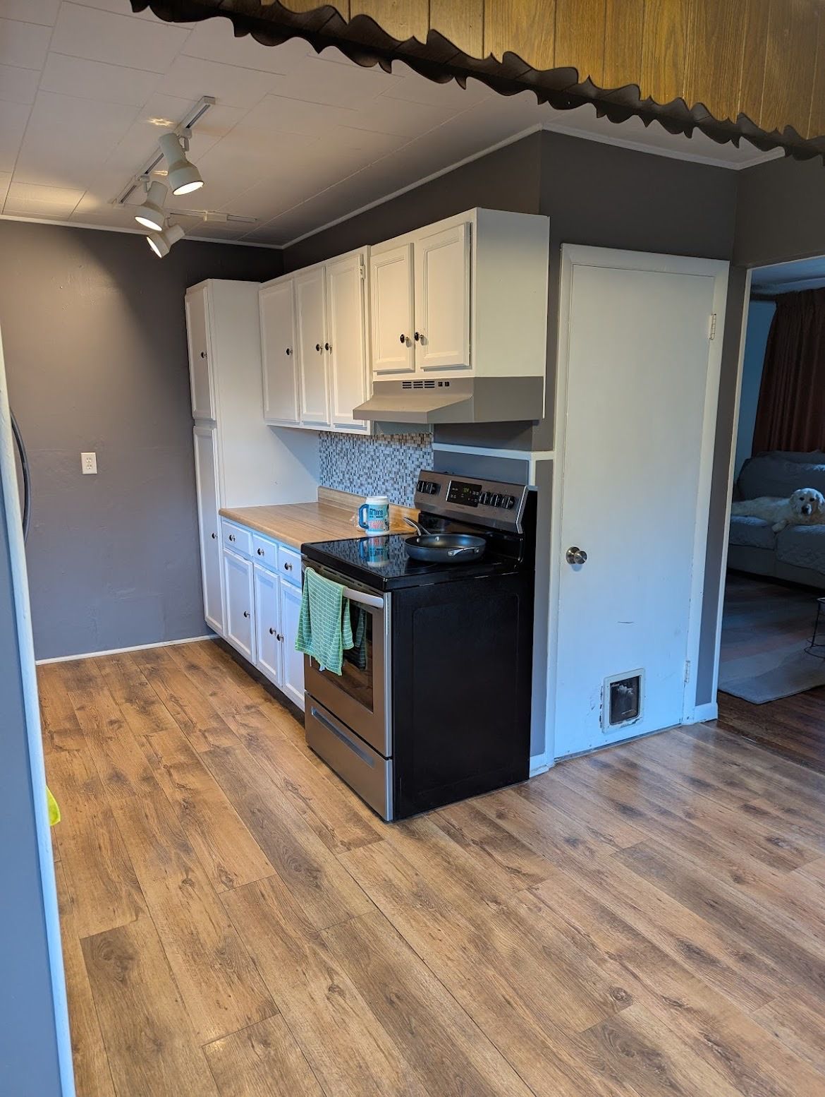 A kitchen with a stove , refrigerator , cabinets and hardwood floors.