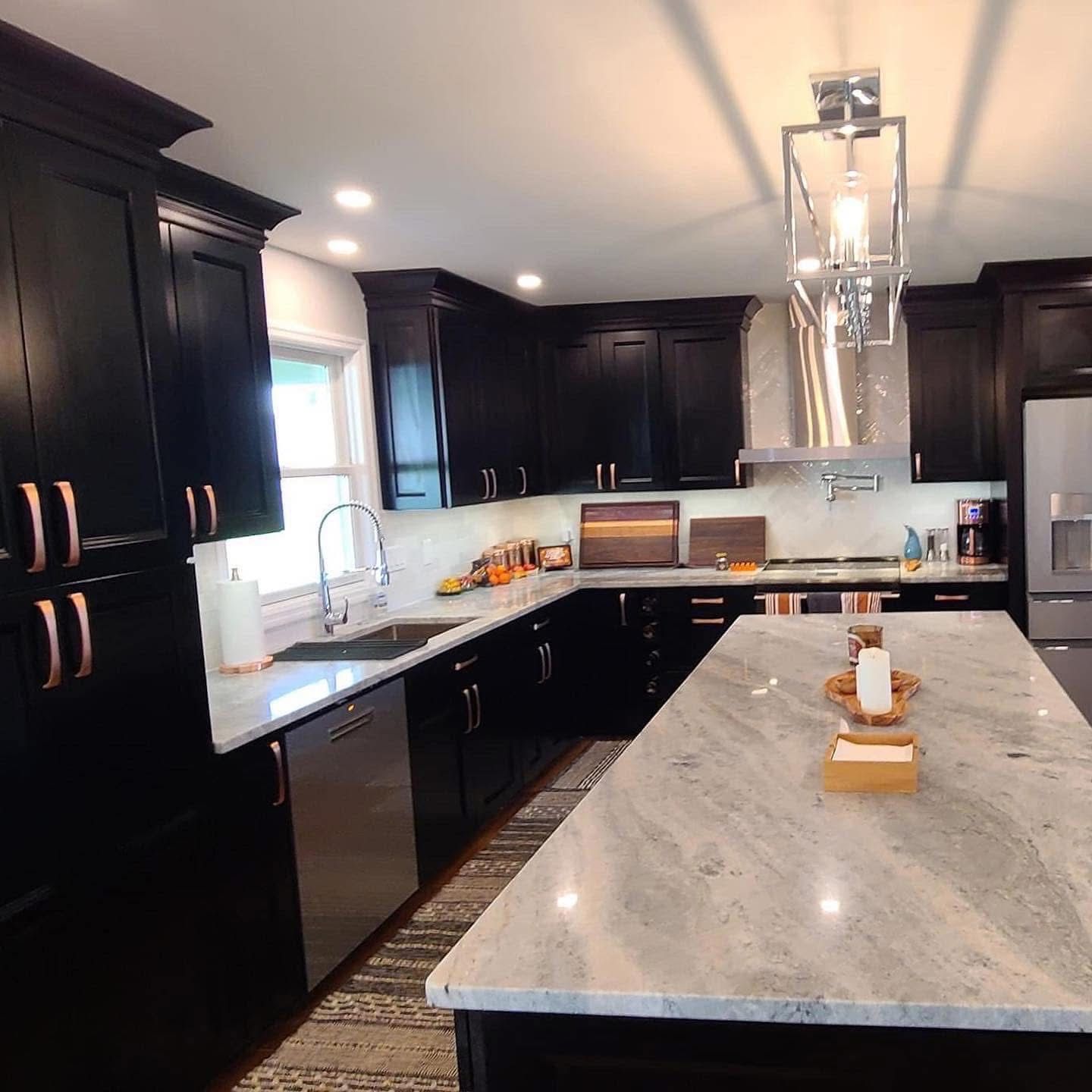A kitchen with black cabinets and a marble counter top