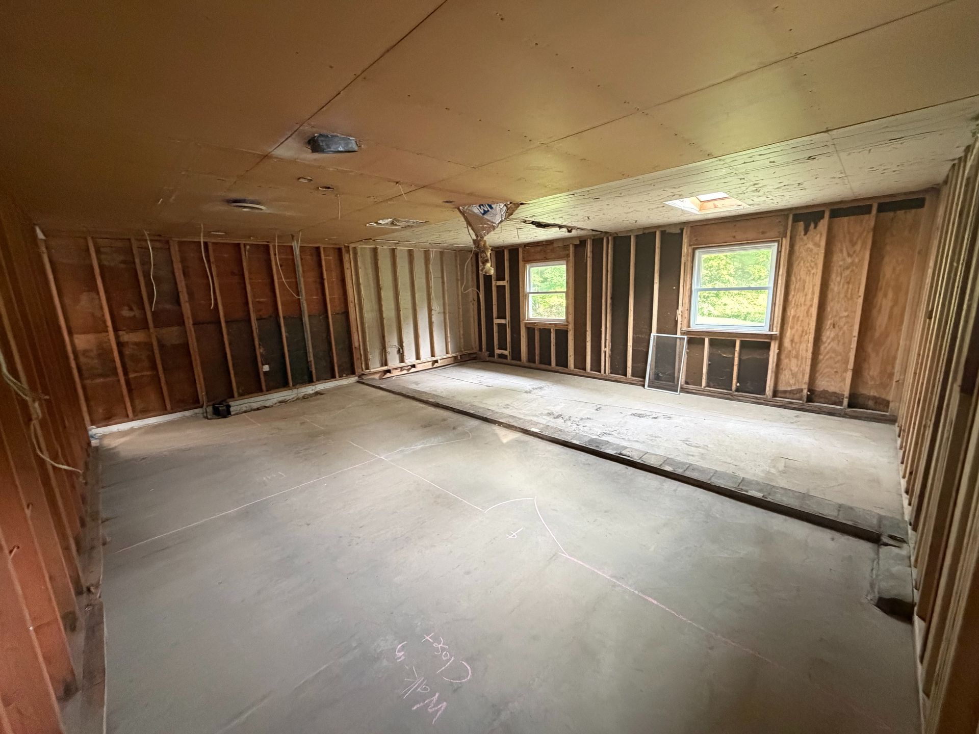 Empty unfinished room with exposed studs, sloped ceiling, and two windows letting in daylight