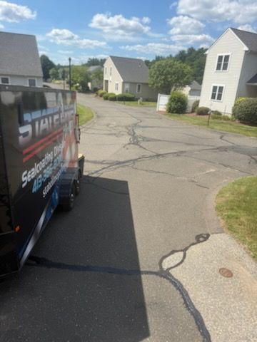 Residential street with cracked pavement beside a van and white houses on a sunny day