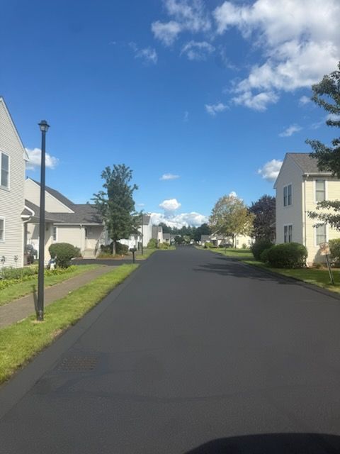 Quiet suburban street with white houses, black pavement, and a bright blue sky with clouds.