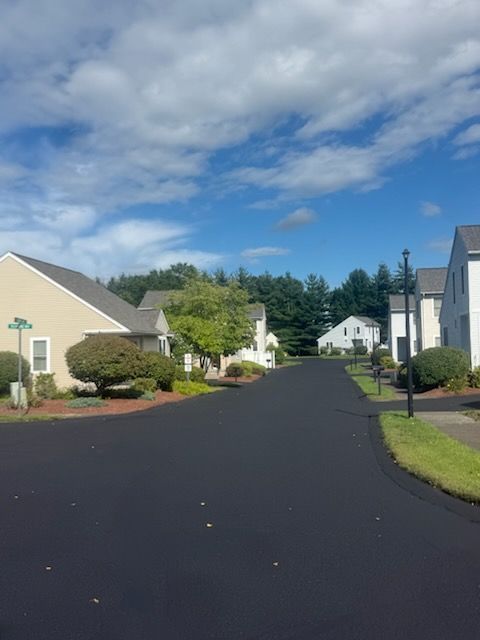 Residential street with houses, dark pavement, and a partly cloudy blue sky