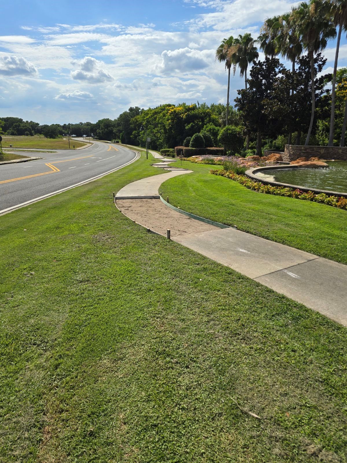 A concrete walkway going through a lush green field next to a road.