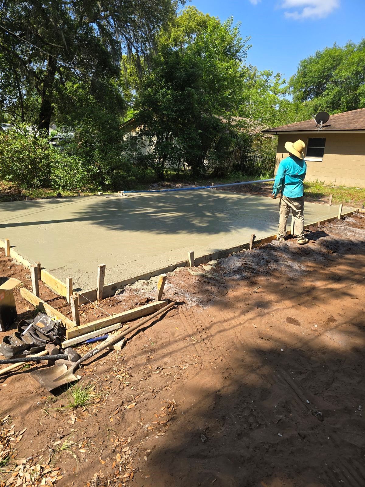 A woman is standing on a dirt road in front of a house.
