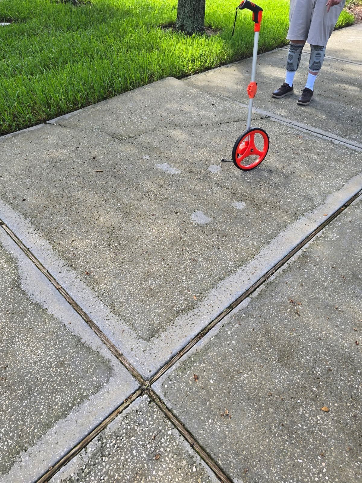 A person is using a measuring wheel on a sidewalk.