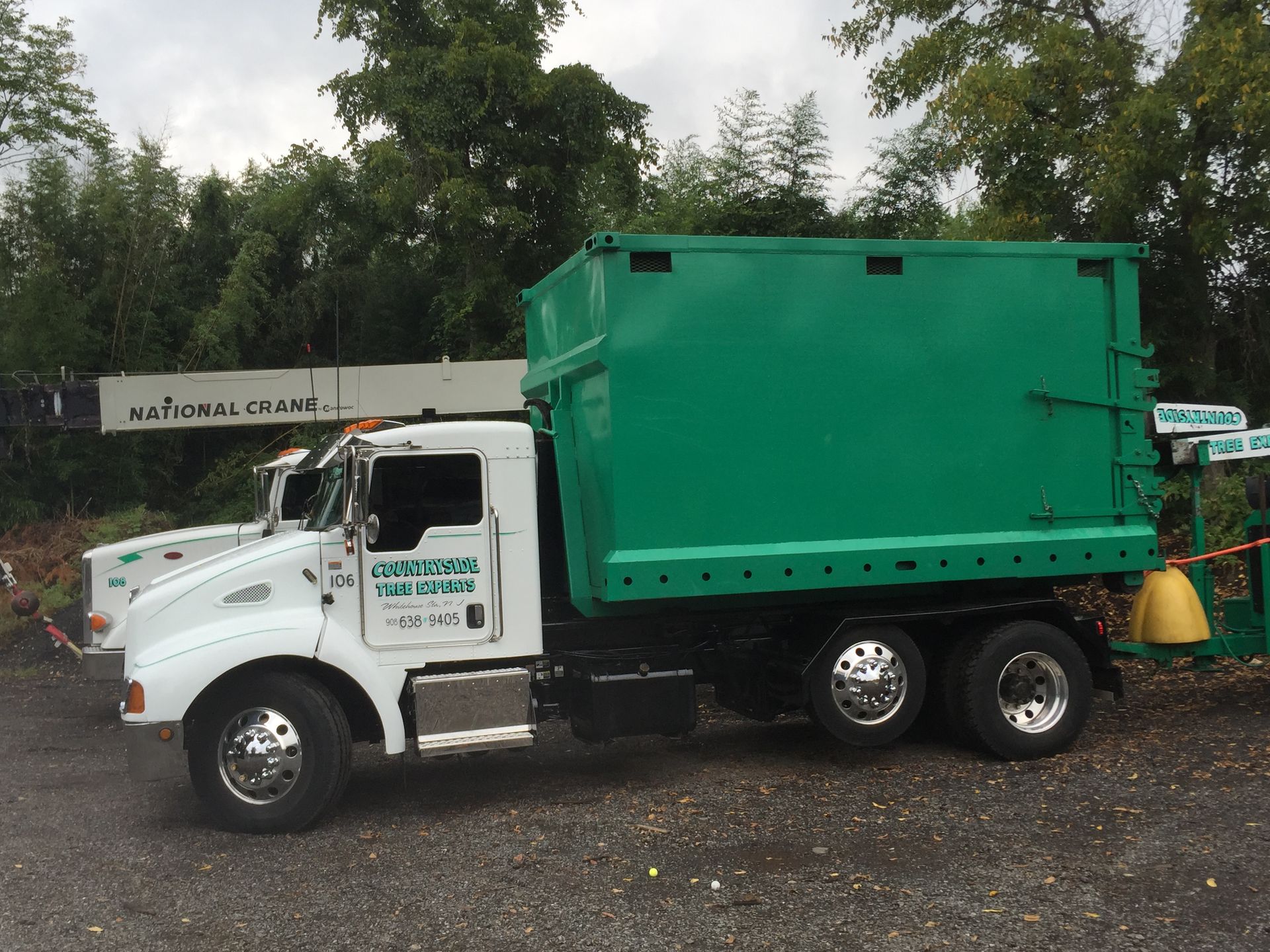 A green and white garbage truck is parked in a gravel lot.