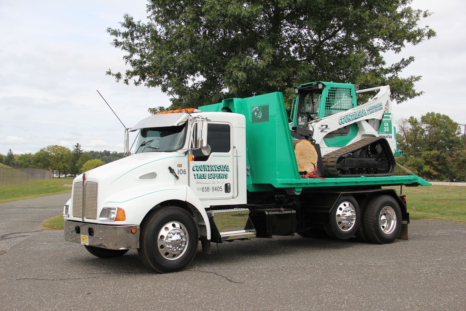 A green and white truck with a tractor on the back is parked on the side of the road.