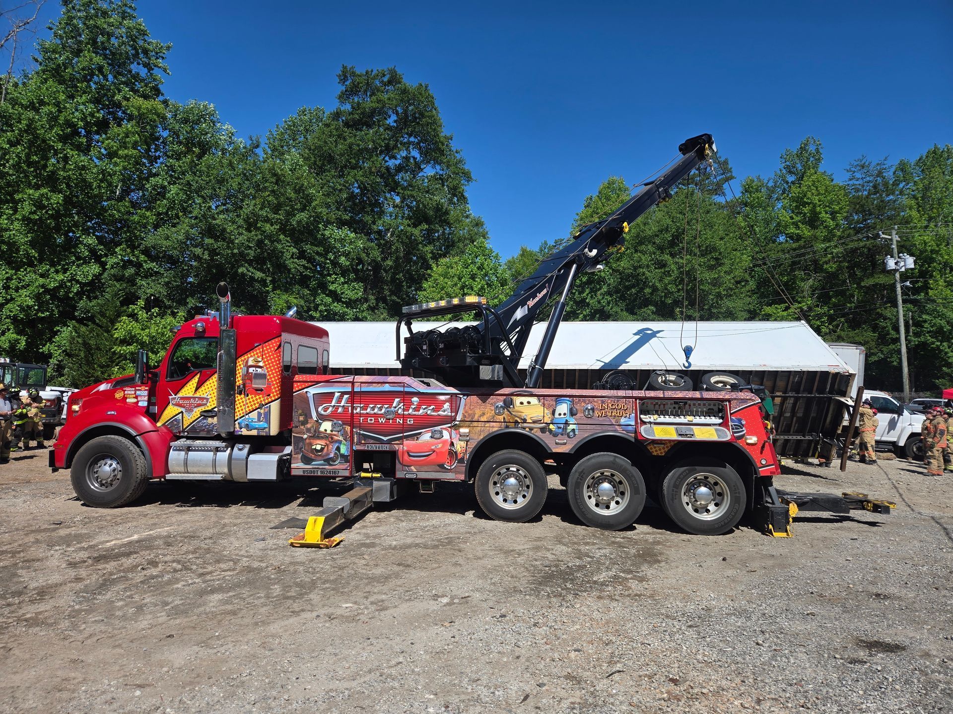 Red tow truck lifting a black sedan on a trailer in a sunny gravel yard