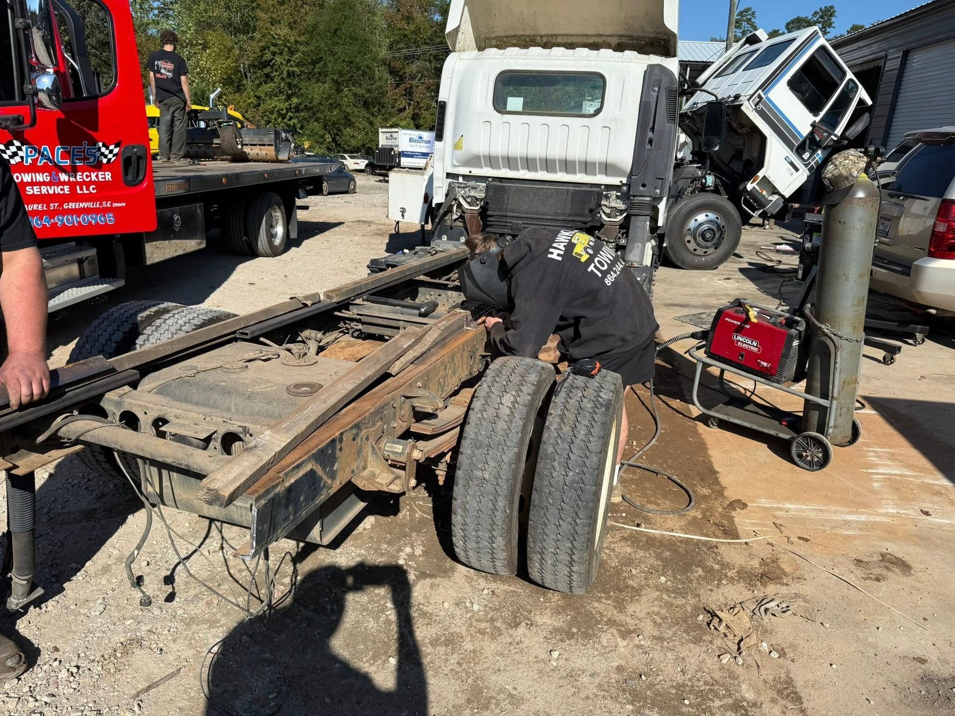 Tow truck crew clearing a wrecked semi-truck chassis and cab on a roadside after a crash