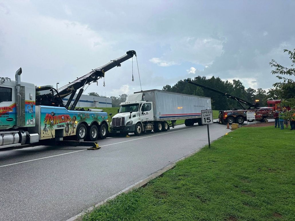 Yellow tow trucks hauling damaged vehicles on a gravel lot with trees and blue sky
