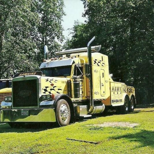 Yellow semi-truck parked on grass under trees, with chrome details and black graphics.