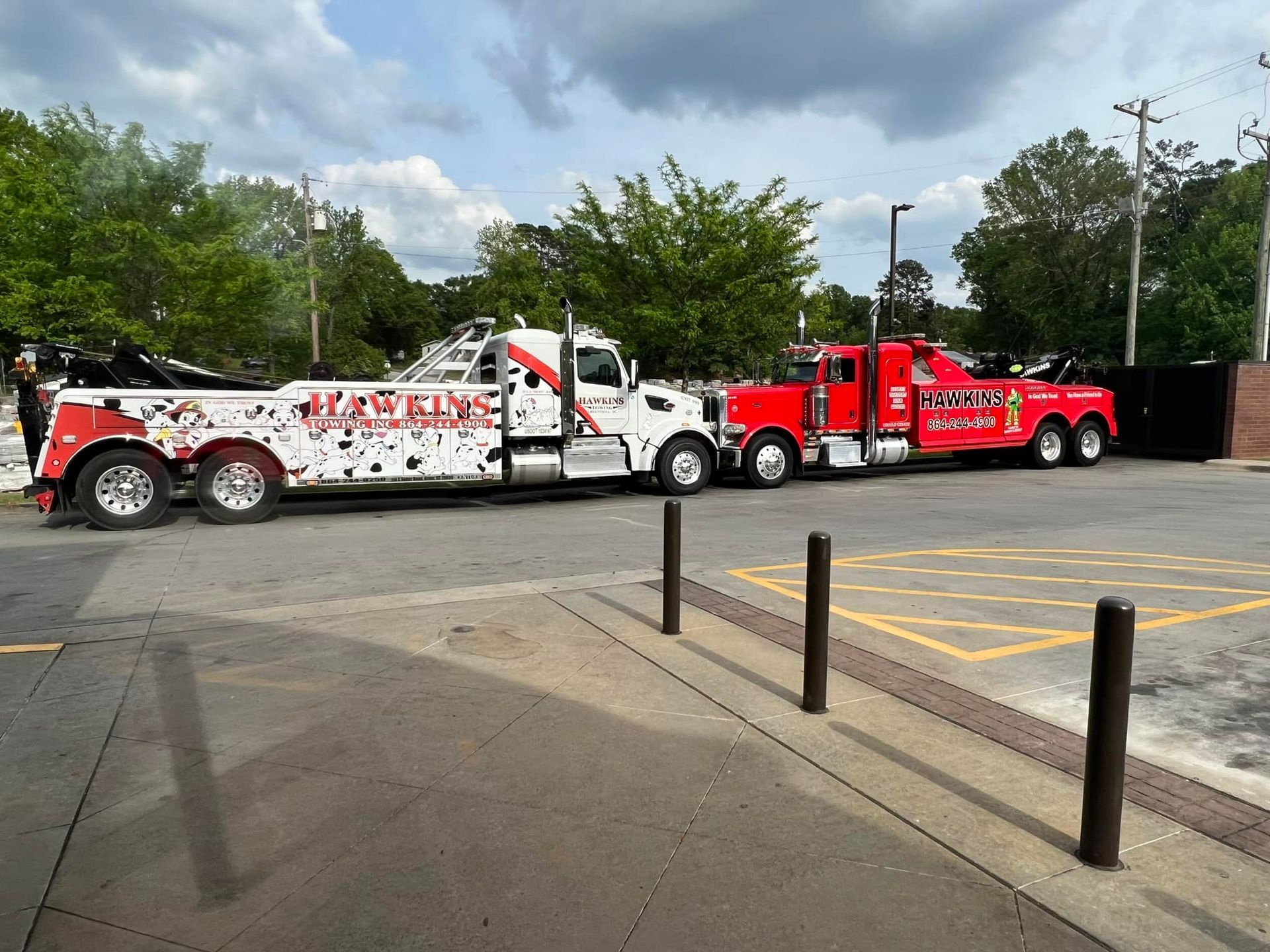 Tow truck and two red service trucks parked in a lot under cloudy skies.