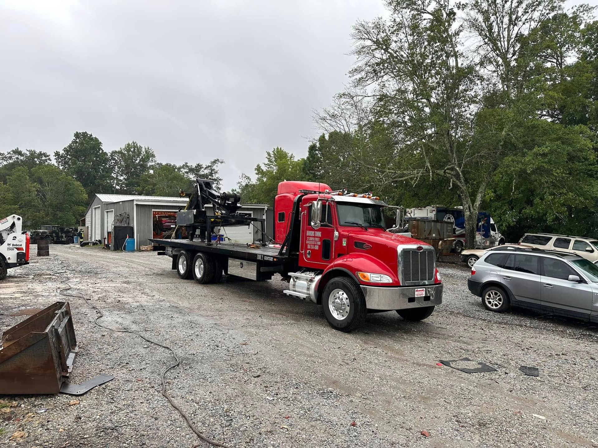 Red tow truck parked on gravel near cars and trees in a lot