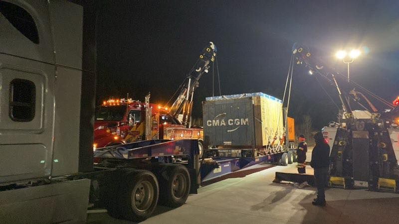 Nighttime truck loading at a port, with a crane lifting a shipping container onto a flatbed trailer.