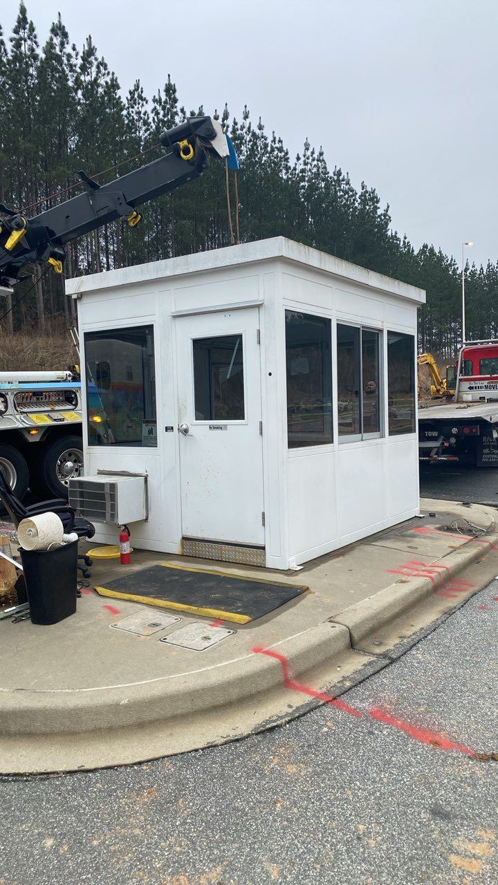 Small white security booth beside a curb at a construction site, with a crane and trucks in the background