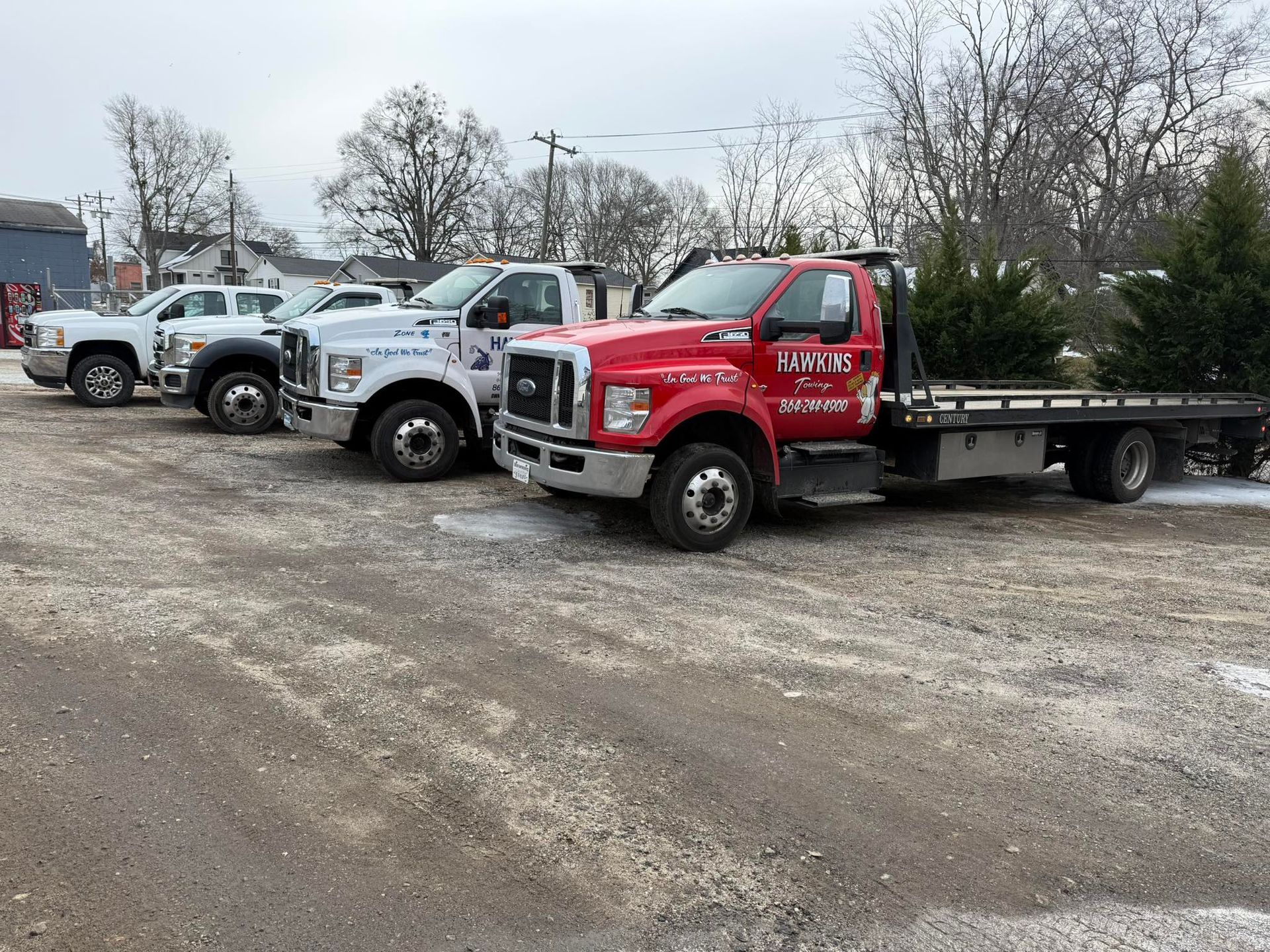 Lineup of tow trucks and work trucks parked on a gravel lot under cloudy skies