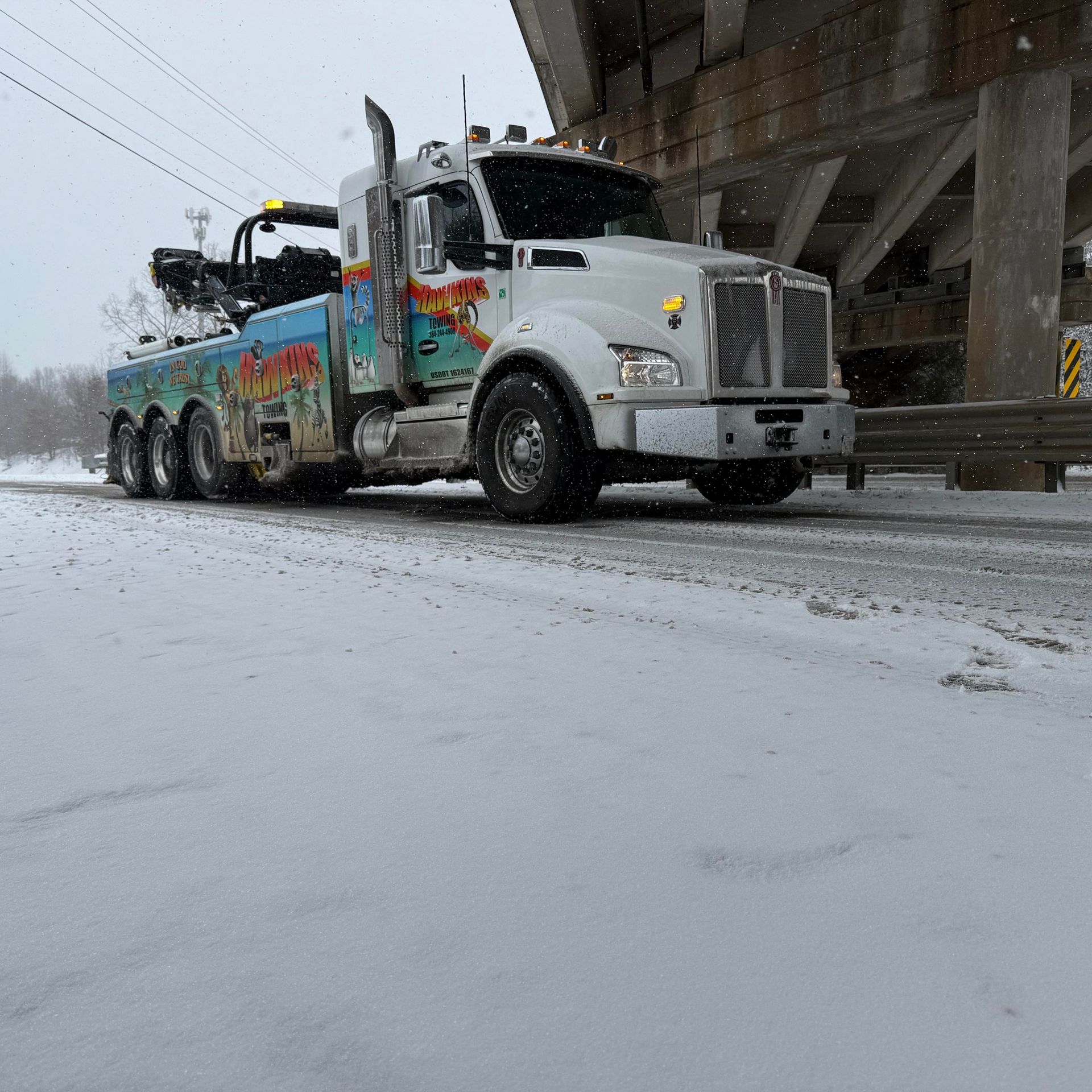 Semi-truck hauling a tanker in snowy weather under an overpass