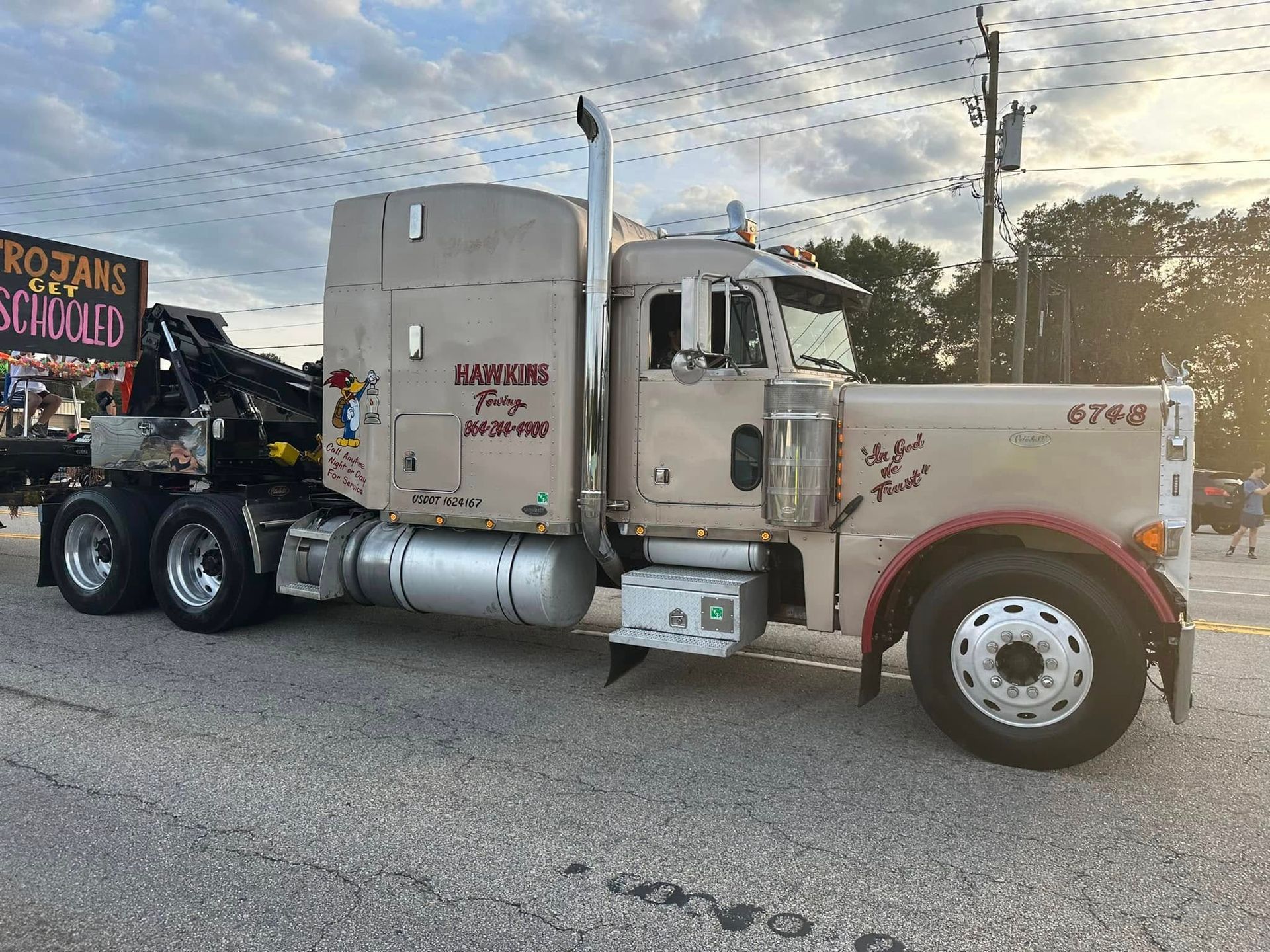 Vintage beige semi truck parked on a roadside at sunset, with a flatbed trailer and signs in the background