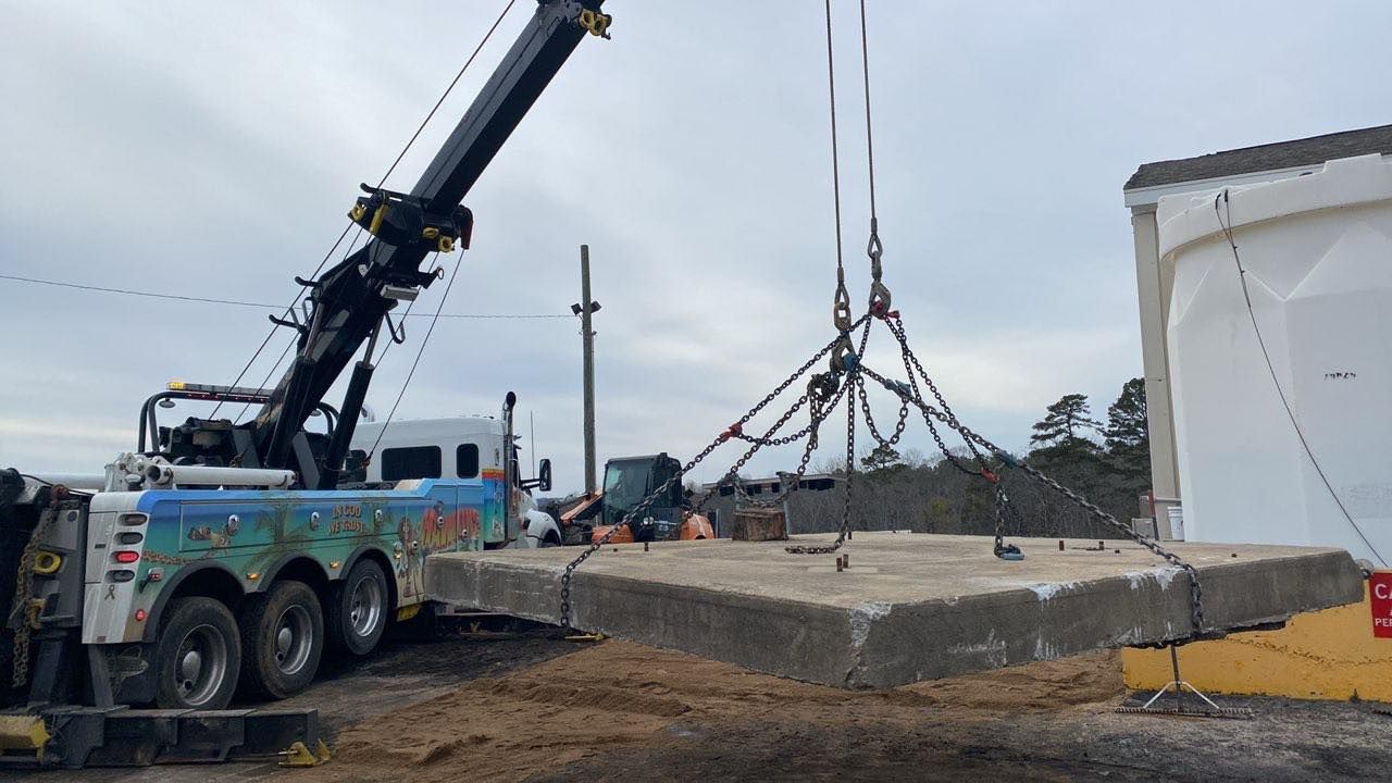 Crane lifting a concrete slab beside a white tent at a construction site under cloudy skies