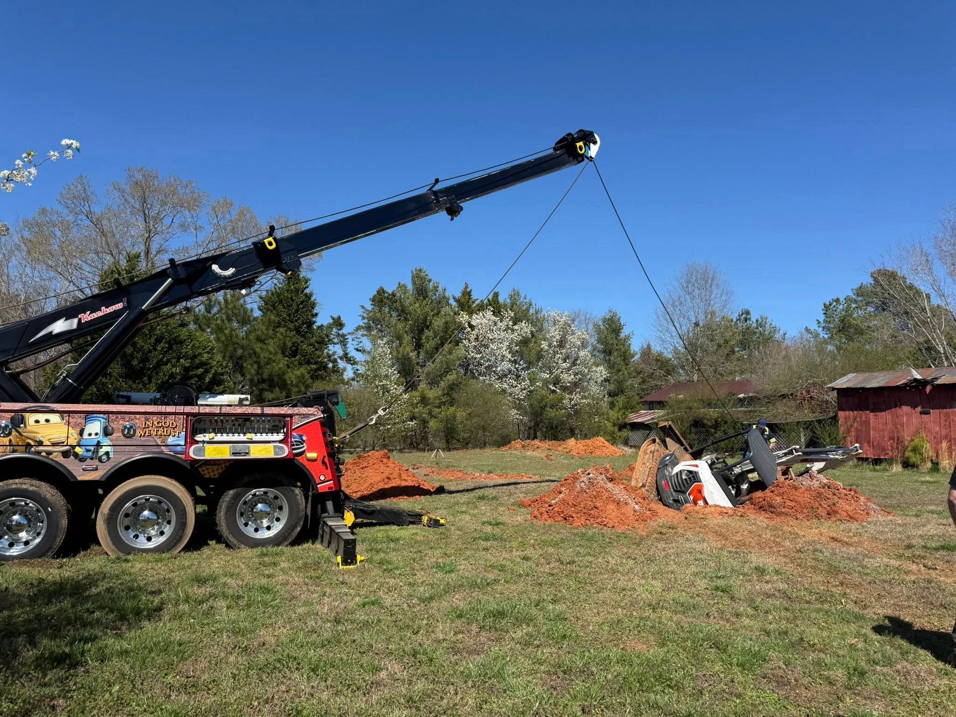 Tow truck lifting a white vehicle from orange debris in a grassy field under a blue sky