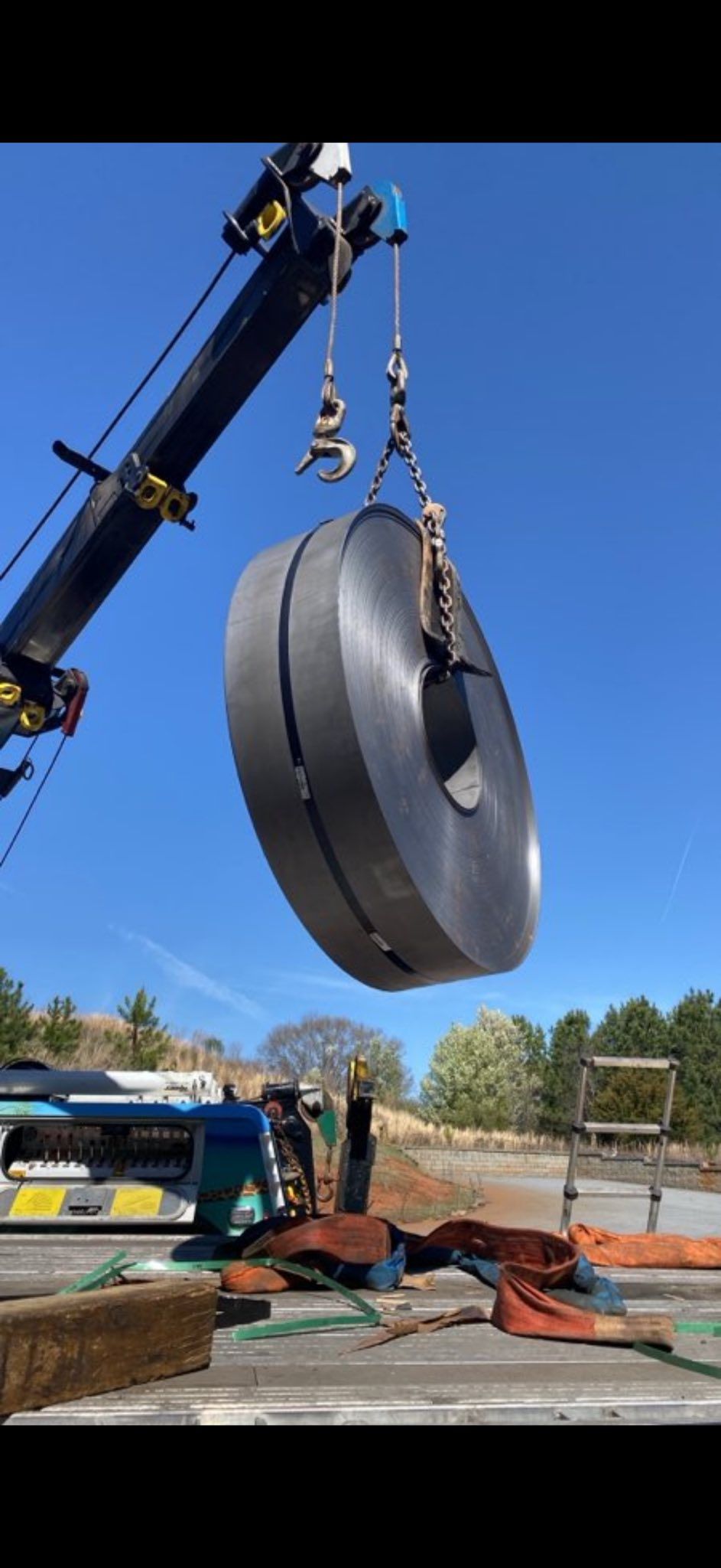 Crane lifting a huge black tire in a yard under a clear blue sky