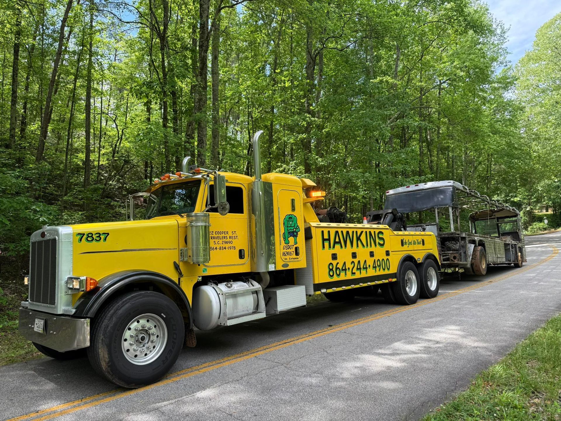 Yellow Hawkins tow truck hauling a flatbed trailer on a forest road