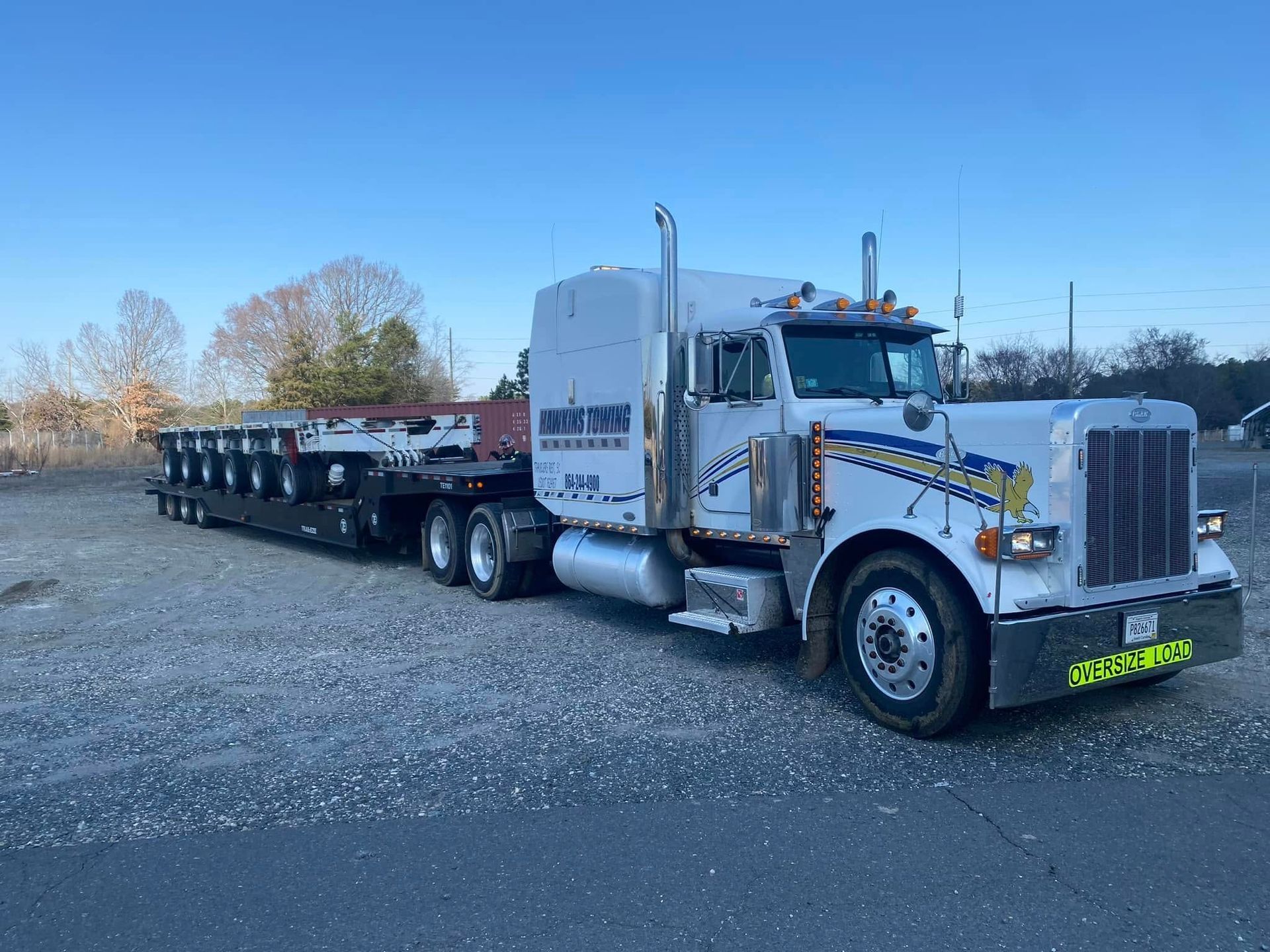 White semi truck hauling an empty flatbed trailer on a gravel lot under a clear sky