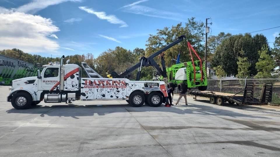 Tow truck loading a green work truck on a flatbed in a parking lot on a sunny day