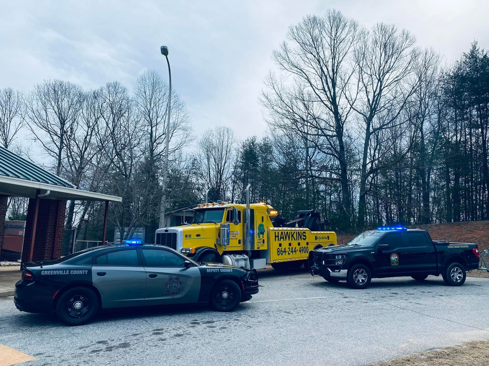 Tow truck towing a black police car on a snowy roadside with a black pickup nearby