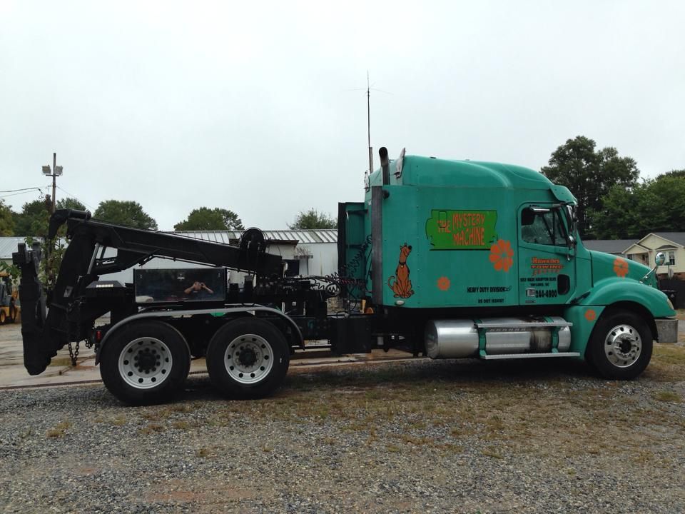 Teal tow truck parked on gravel lot, side view.