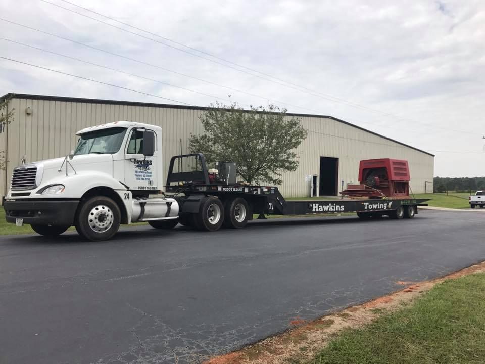 White semi-truck hauling a red truck trailer on a paved lot under a cloudy sky