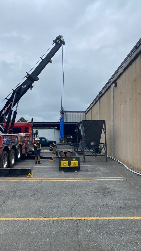Crane lifting a large blue container beside a warehouse loading area under an overcast sky