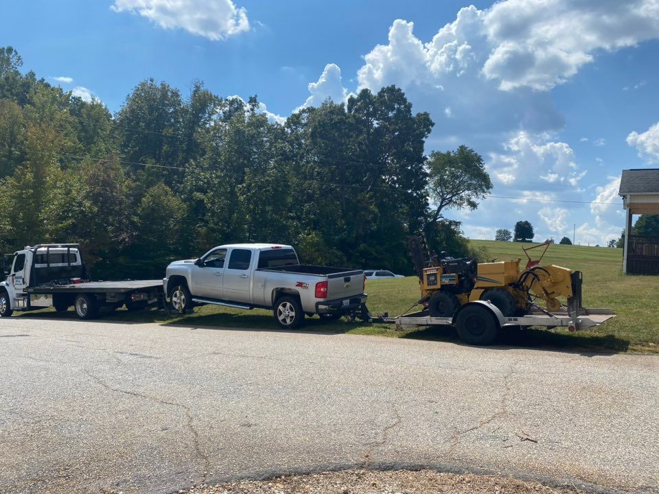 Pickup truck towing a yellow wood chipper on a trailer beside a grassy field and trees under a blue sky